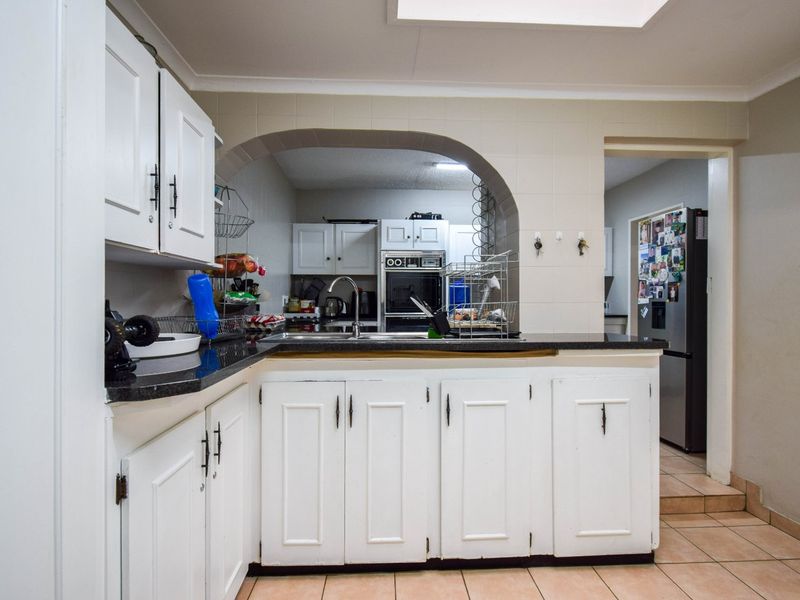 A functional kitchen featuring white cabinetry, granite countertops, and a built-in oven, connected to an adjacent space via a classic architectural archway.