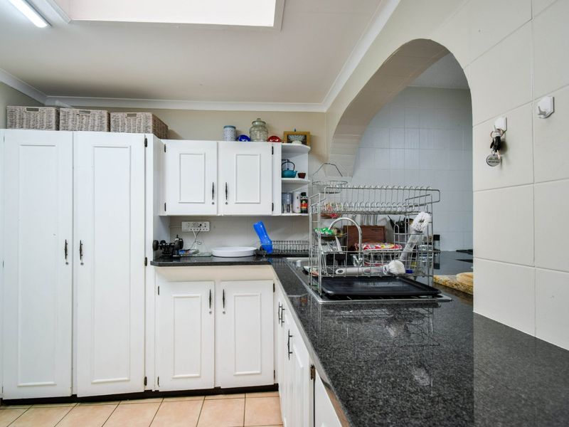 A functional kitchen featuring white cabinetry, dark granite countertops, a double sink, and tiled flooring, connected to an adjacent space via an archway.