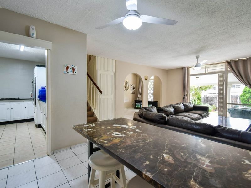 Open plan living and dining area featuring tiled floors, ceiling fans, and an adjacent kitchen with built-in cabinetry and appliances.