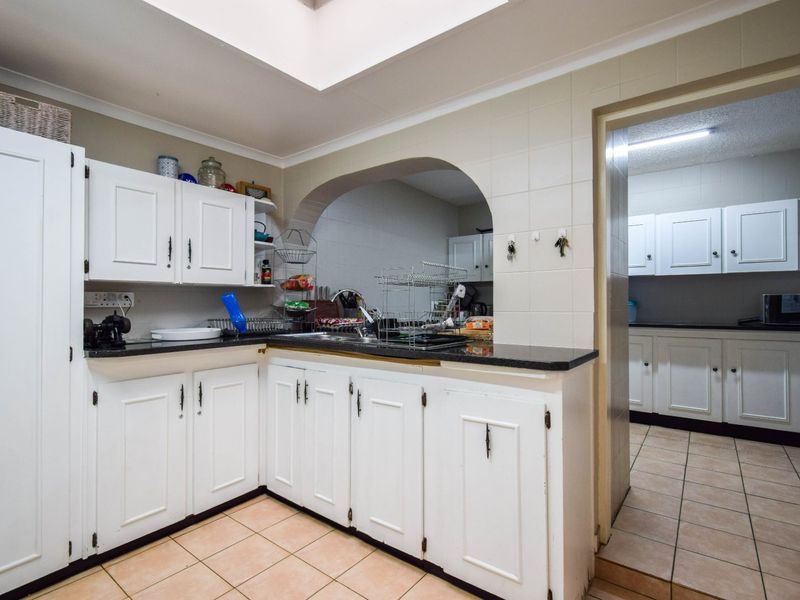 Functional kitchen featuring granite countertops, white cabinetry, a double basin sink, and a skylight, with an adjacent scullery area.