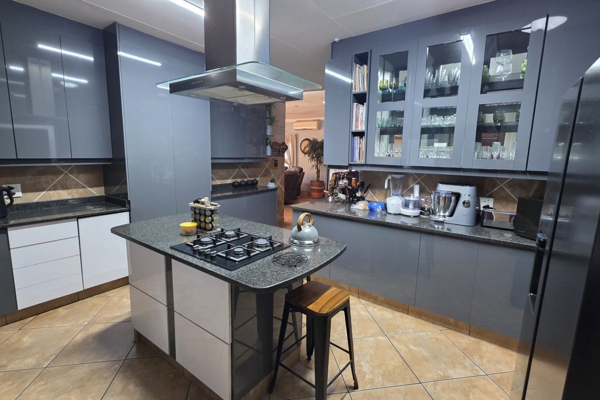 Modern kitchen featuring a central island with gas cooktop, granite countertops, ample grey cabinetry, and glass-fronted display units.