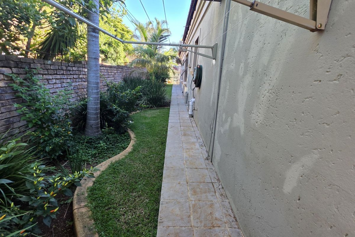 A side garden pathway featuring a tiled walkway, brick boundary wall, and wall-mounted washing line along the exterior of the property.
