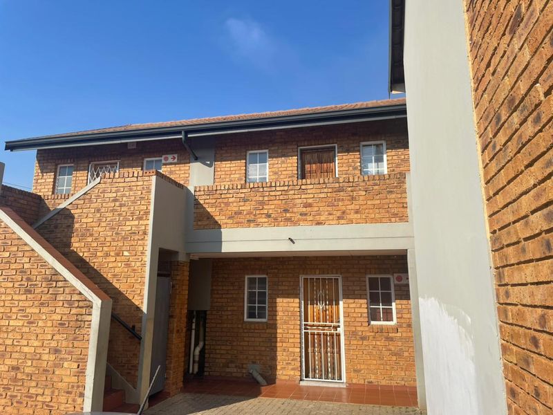 Exterior view of a face brick apartment building featuring an external staircase, security gate entrance, and a tiled patio area.