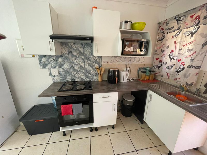 Compact kitchen featuring built-in oven, electric hob, extractor fan, laminate countertops, and stainless steel sink with tiled flooring and cabinetry.
