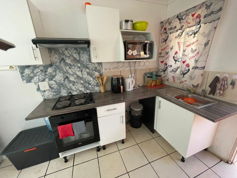 Compact kitchen featuring white cabinetry, laminate countertops, built-in oven, electric hob, extractor fan, and tiled flooring.