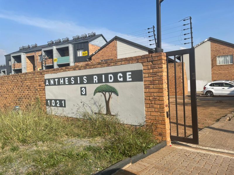 Entrance view of Anthesis Ridge apartment complex featuring a brick boundary wall, electric fencing, and paved access gate.