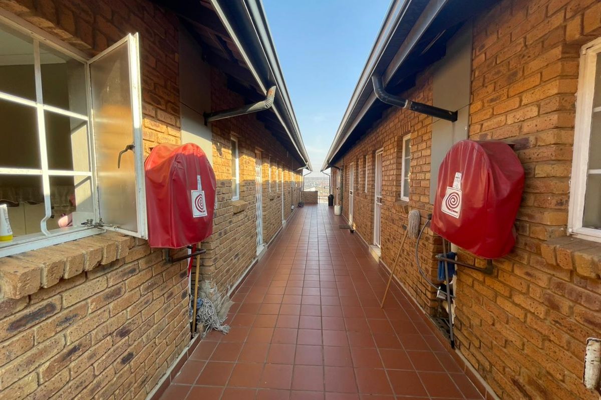 An exterior apartment hallway featuring exposed brick walls, tiled flooring, and wall-mounted fire hose reels.