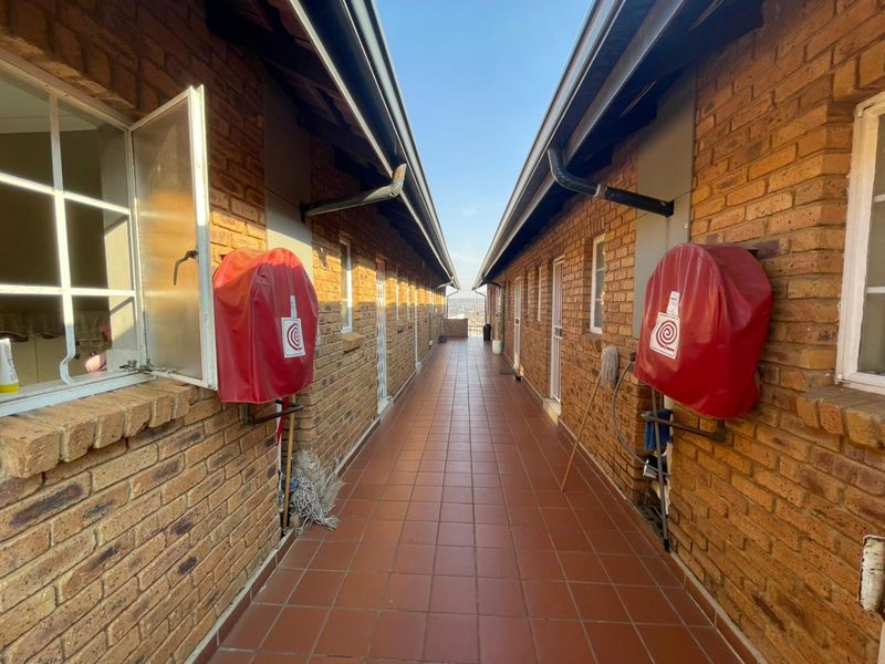 An exterior apartment hallway featuring exposed brick walls, tiled flooring, and wall-mounted fire hose reels.