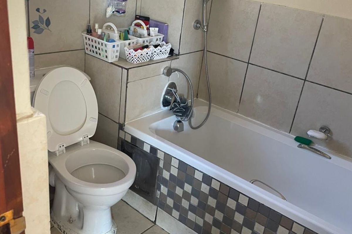 A compact bathroom featuring a bathtub with a handheld shower mixer, a standard toilet, and neutral wall and floor tiling.