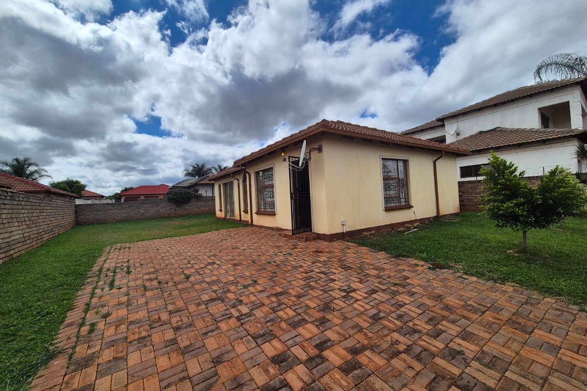 Rear view of the property featuring a paved courtyard, lawn area, and brick boundary walls under a tiled roof structure.