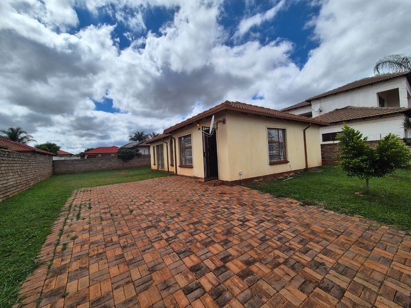 Rear view of the property featuring a paved courtyard, lawn area, and brick boundary walls under a tiled roof structure.