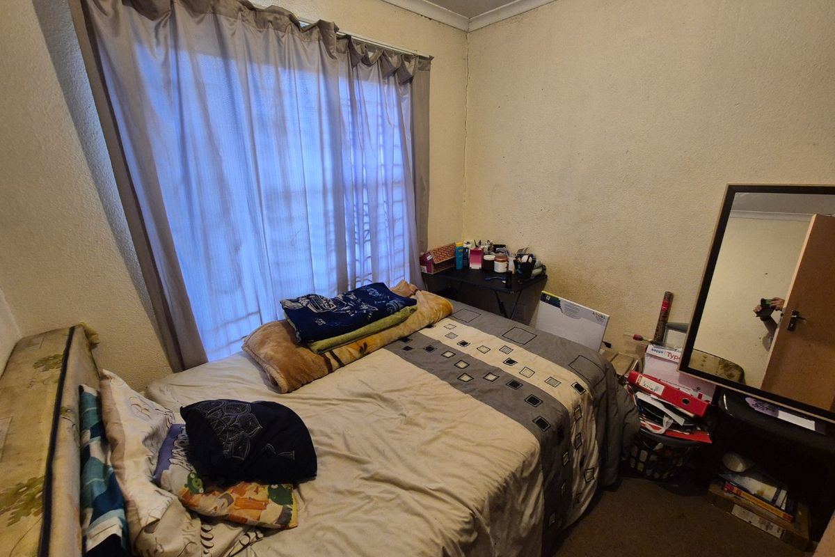A bedroom featuring a window with curtain rails and coving, currently showing signs of significant wear and wall surface deterioration.
