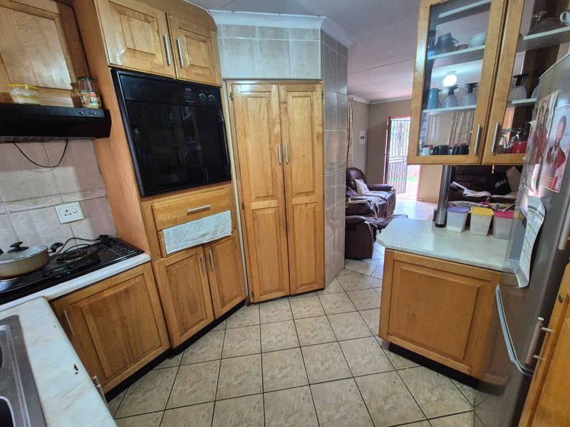 A functional kitchen featuring wooden cabinetry, tiled flooring, and built-in appliances, offering a traditional layout with direct access to the adjacent living area.