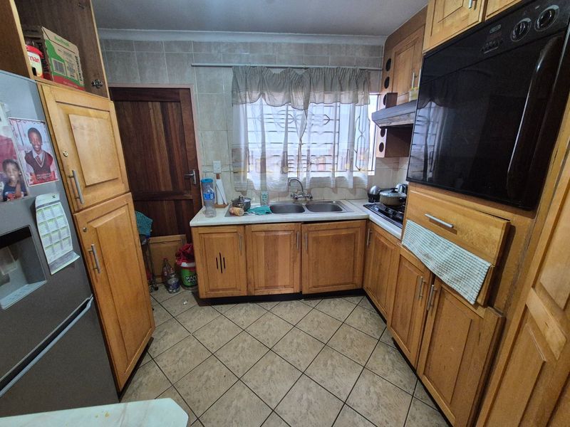 A functional kitchen featuring wooden cabinetry, a double basin sink, built-in oven, and tiled finishes throughout.