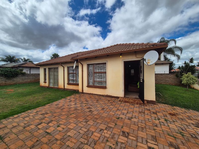 Rear view of the house featuring a paved patio area, tiled roof, and secure window bars, set within a private garden with boundary walls.