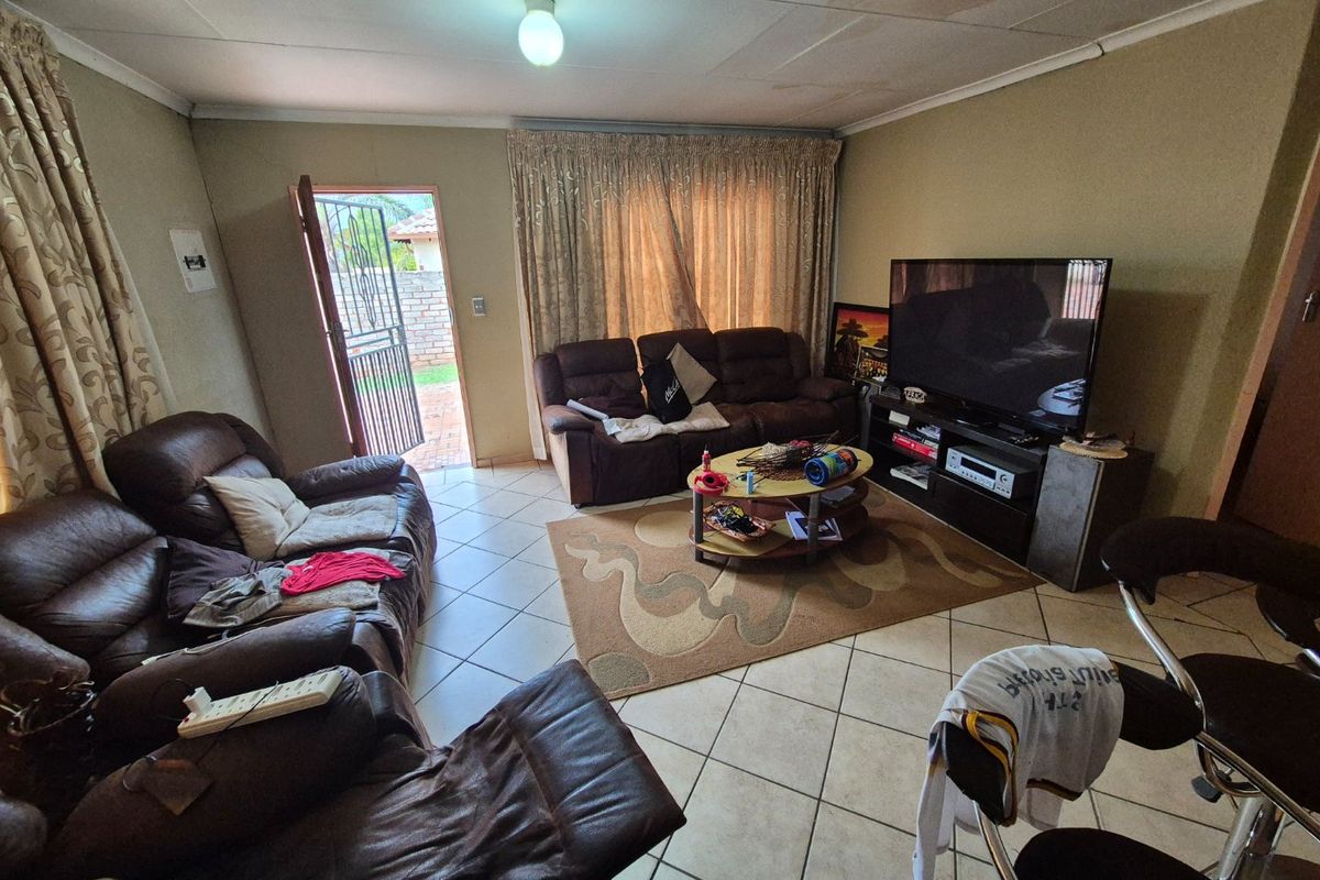 A living room featuring tiled flooring and direct access to the exterior, showing signs of ceiling wear and water staining.