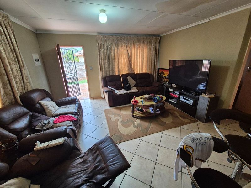 A living room featuring tiled flooring and direct access to the exterior, showing signs of ceiling wear and water staining.