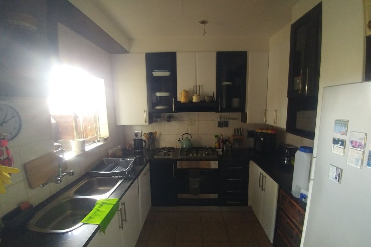 A functional kitchen featuring dark and light cabinetry, a gas hob, built-in oven, and double bowl sink with tiled splashbacks.