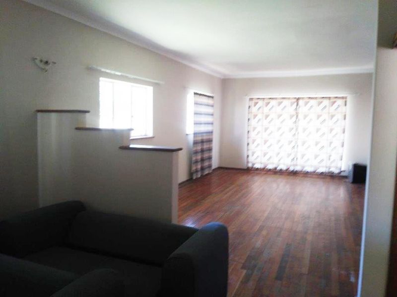 A spacious living room featuring polished hardwood flooring, a coved ceiling, and a unique half-height partition wall, offering a bright and open layout.