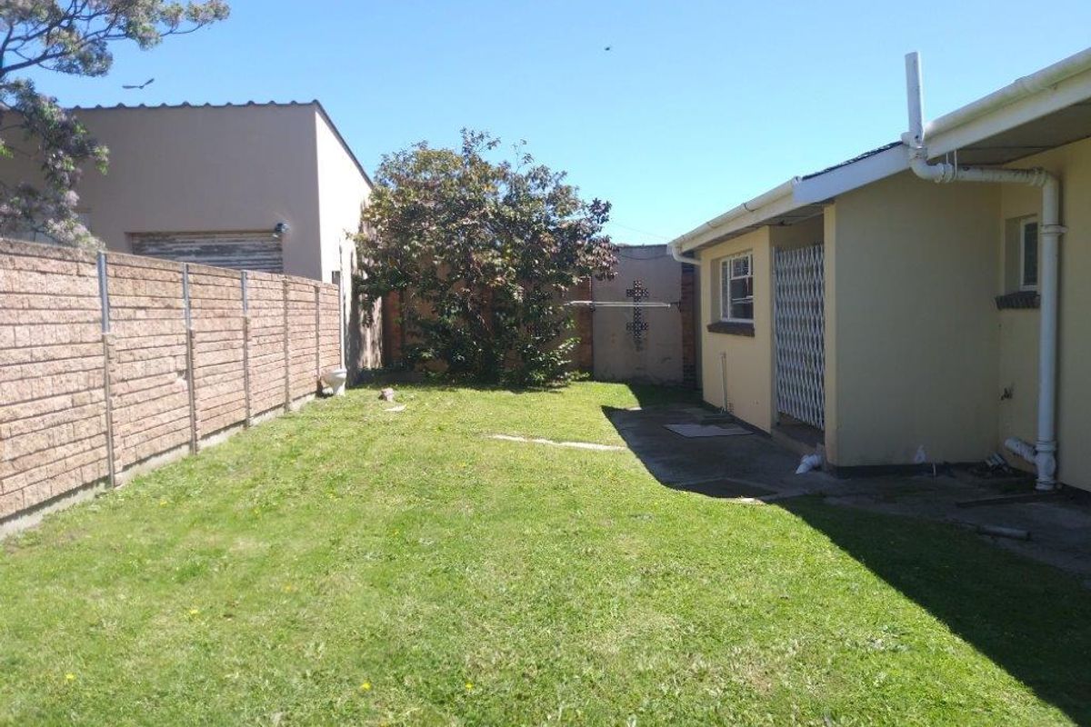 A rear garden area featuring a lawn, brick boundary wall, and a concrete patio space adjacent to the house structure.