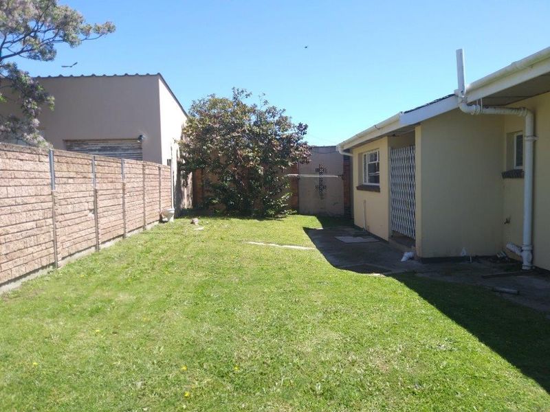 A rear garden area featuring a lawn, brick boundary wall, and a concrete patio space adjacent to the house structure.