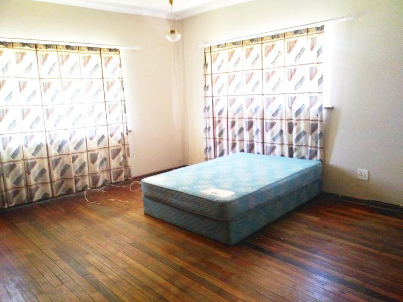 A bedroom featuring original hardwood flooring, dual windows with curtain rails, and neutral wall paint, offering a blank canvas for renovation.