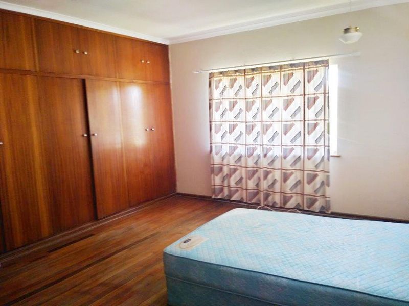 A bedroom featuring original wooden flooring and extensive built-in wooden cabinetry, offering ample storage space in a neutral setting.