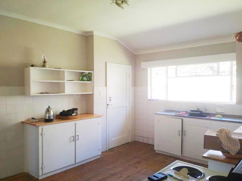 A functional kitchen featuring built-in cabinetry, a tiled splashback, and a sink, offering a practical layout with potential for modern updates.