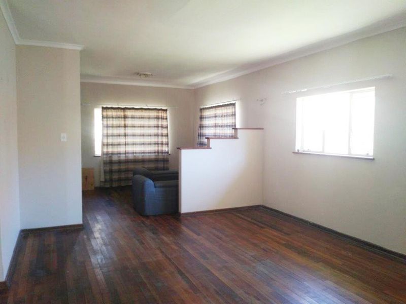 Spacious living area featuring original hardwood flooring, a central half-height partition wall, and neutral wall tones.