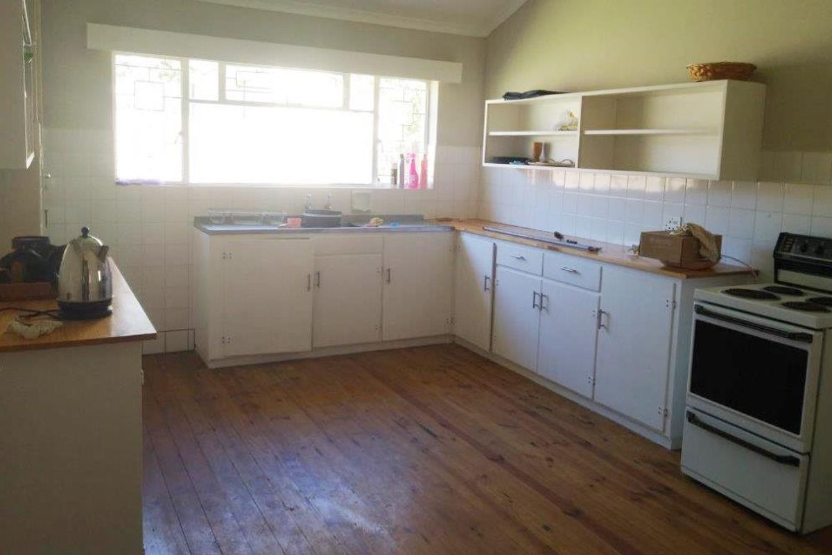 A functional kitchen featuring timber flooring, white built-in cabinetry, tiled splashbacks, and a freestanding stove, offering potential for modern renovation.