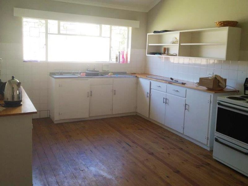 A functional kitchen featuring timber flooring, white built-in cabinetry, tiled splashbacks, and a freestanding stove, offering potential for modern renovation.
