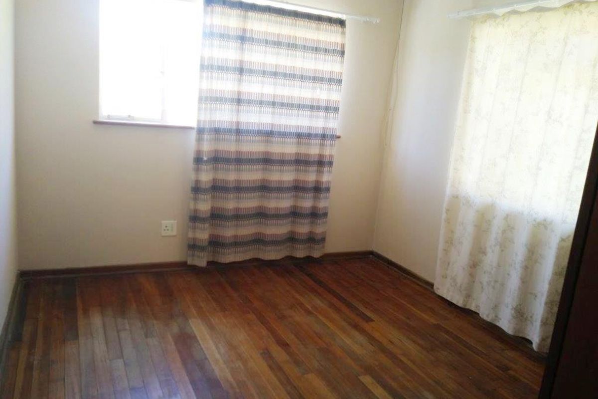 An empty bedroom featuring original hardwood flooring and dual windows, providing a blank canvas for personalization.