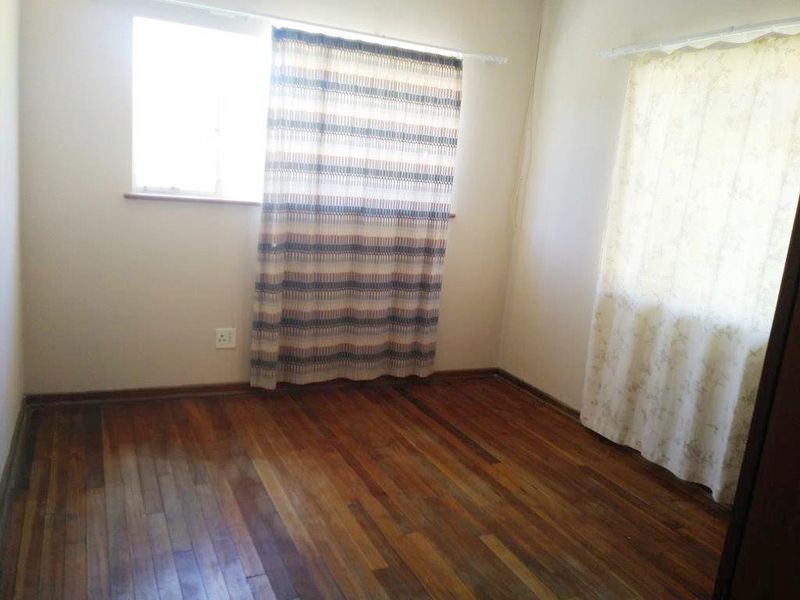 An empty bedroom featuring original hardwood flooring and dual windows, providing a blank canvas for personalization.