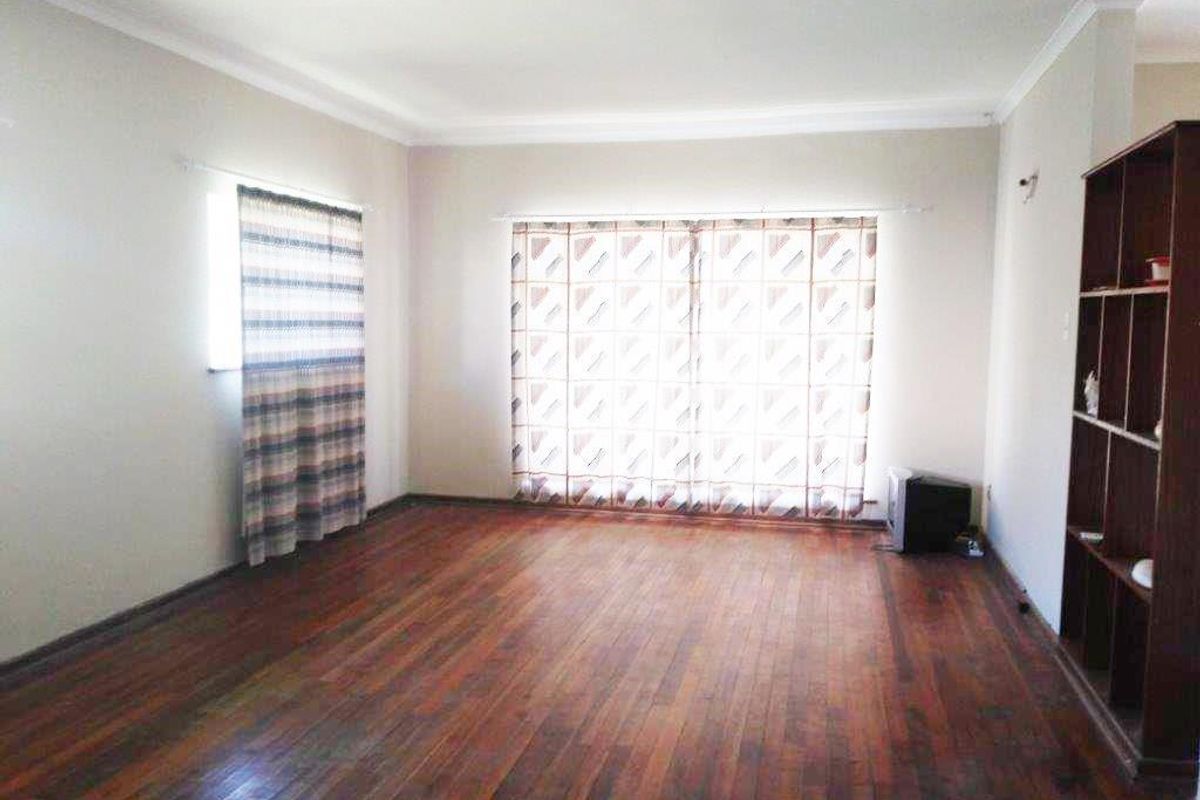 Spacious living room featuring polished hardwood flooring, neutral walls, and a built-in wooden shelving unit, offering a bright and versatile living space.