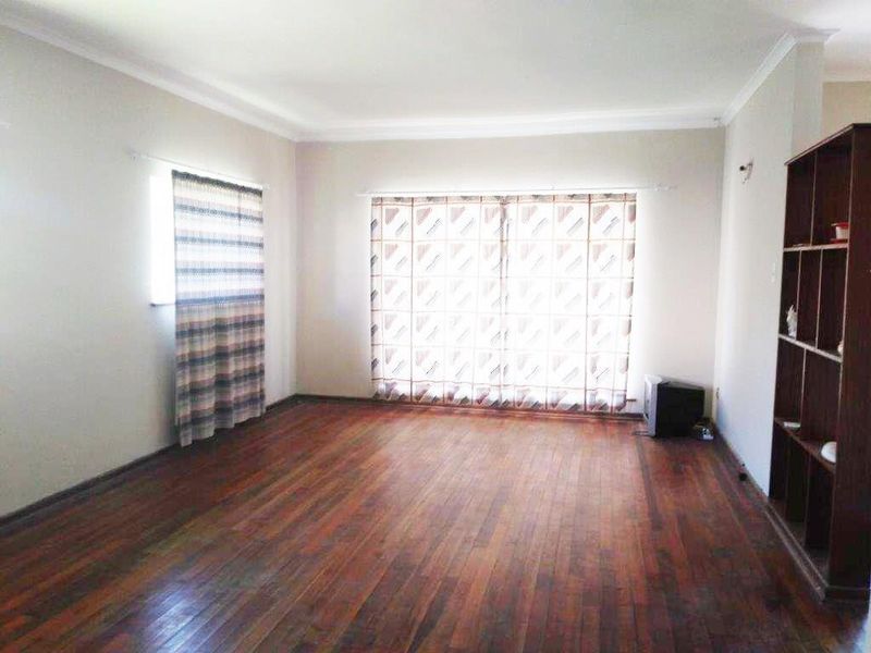Spacious living room featuring polished hardwood flooring, neutral walls, and a built-in wooden shelving unit, offering a bright and versatile living space.