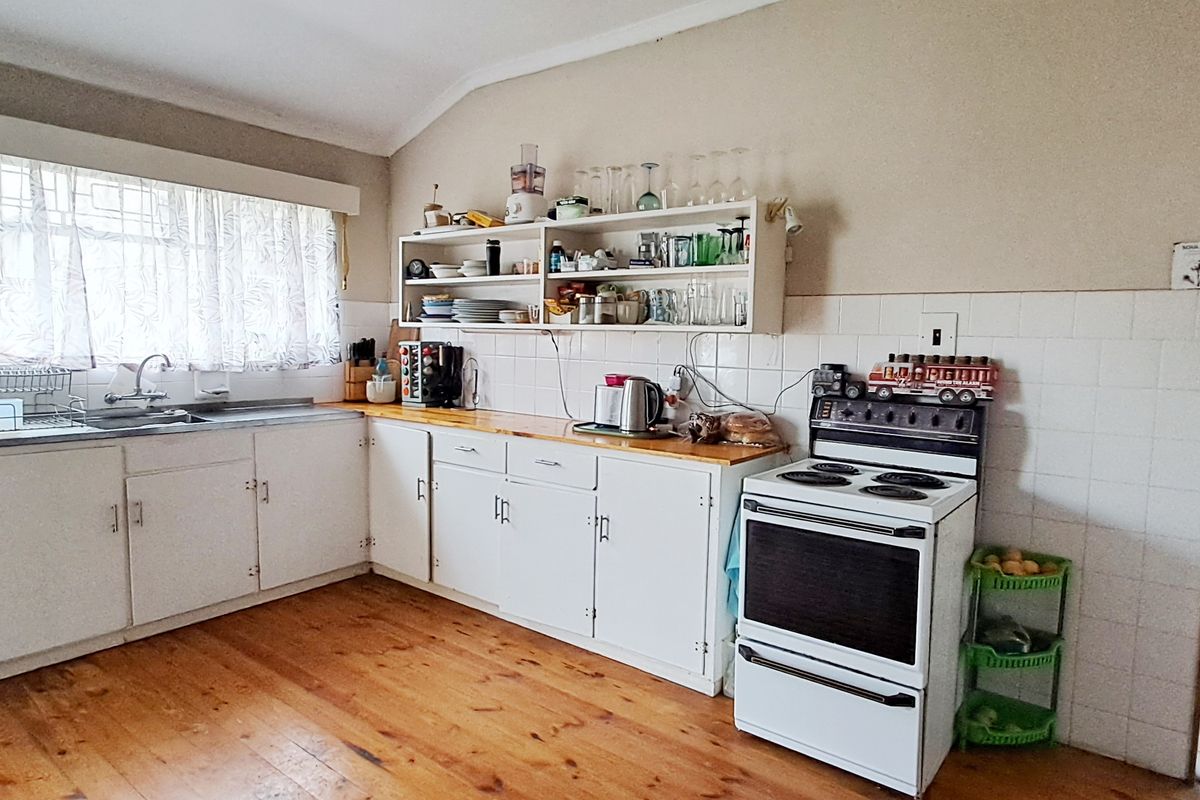 A functional kitchen featuring timber flooring, white cabinetry, wooden countertops, a tiled splashback, and a freestanding stove.