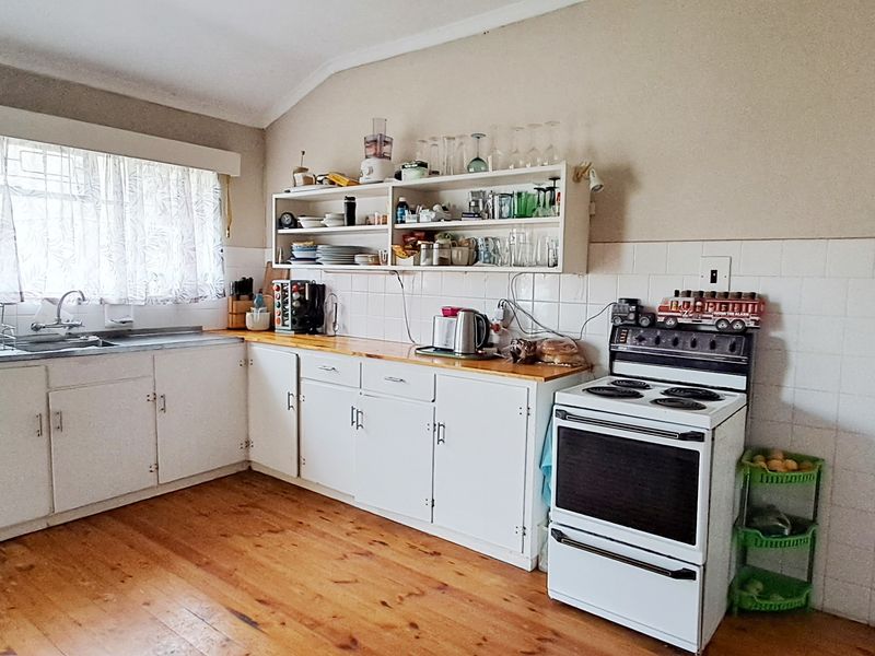 A functional kitchen featuring timber flooring, white cabinetry, wooden countertops, a tiled splashback, and a freestanding stove.