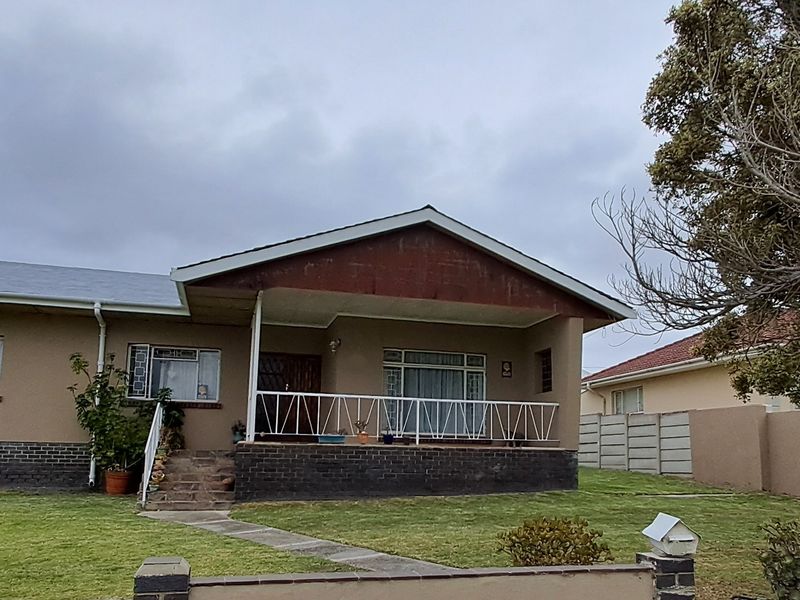 A single-story residential home featuring a covered front porch, brick foundation, and a spacious front lawn with established trees and boundary walling.