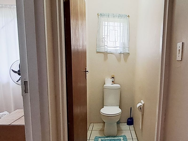 A functional, compact guest toilet featuring tiled flooring and a window with security bars.