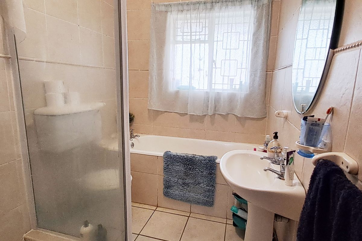 A functional bathroom featuring a shower enclosure, bathtub, and pedestal washbasin with neutral wall and floor tiling.