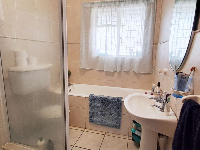 A functional bathroom featuring a shower enclosure, bathtub, and pedestal washbasin with neutral wall and floor tiling.