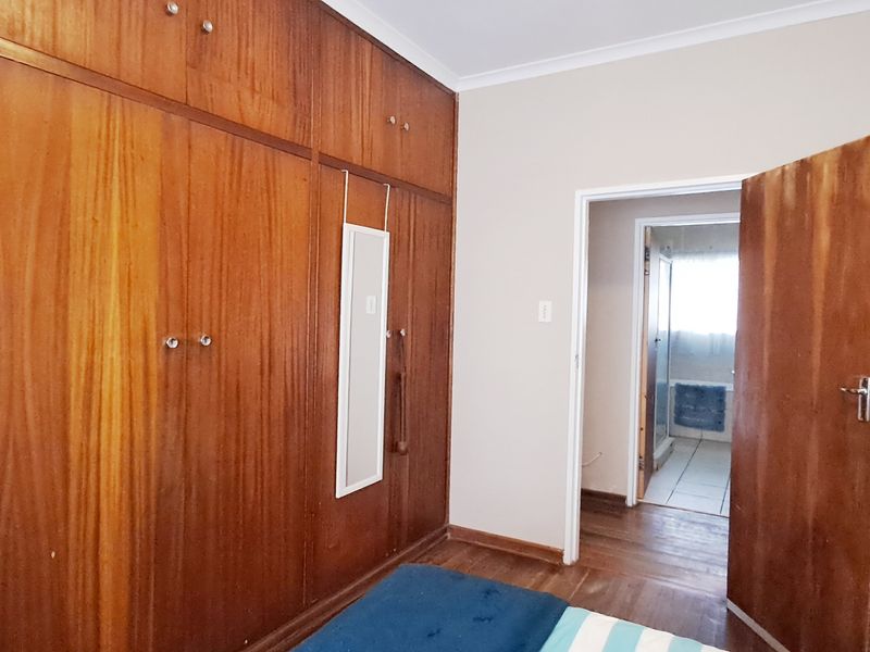 Bedroom featuring extensive built-in wooden cabinetry, warm timber flooring, and direct access to an adjoining bathroom.