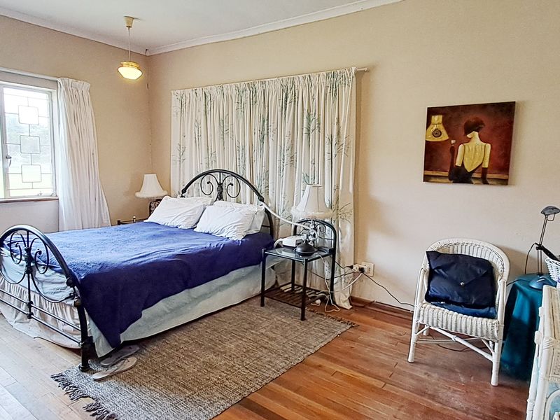 A spacious bedroom featuring original hardwood flooring and a large window, offering a blank canvas for potential interior updates and modernization.
