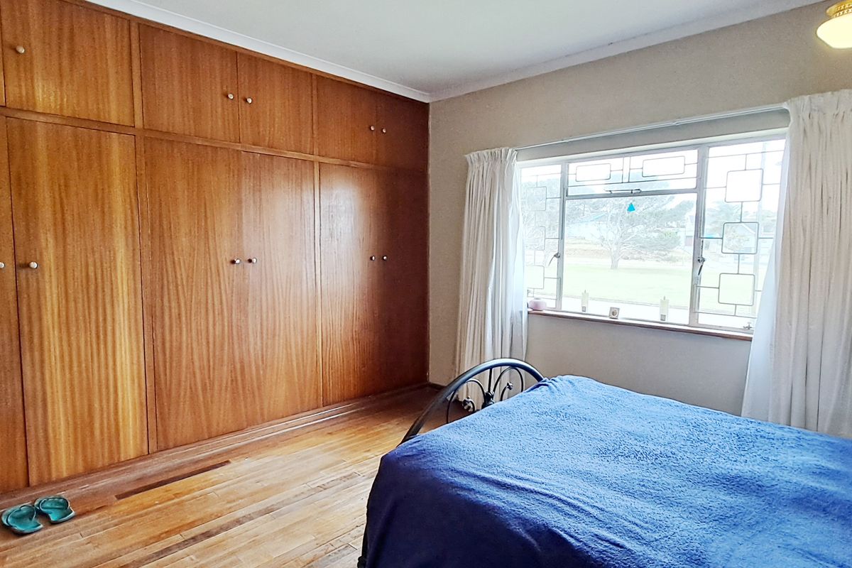 A bedroom featuring extensive floor-to-ceiling built-in wooden cabinetry, original hardwood flooring, and a large steel-framed window providing natural light.