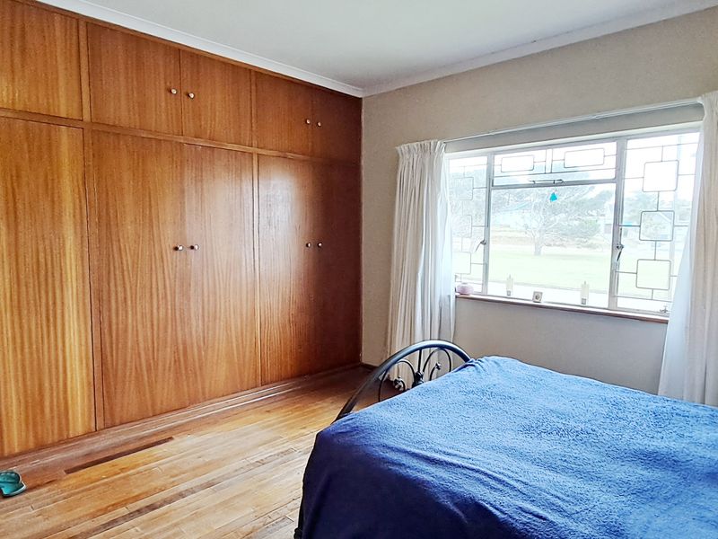 A bedroom featuring extensive floor-to-ceiling built-in wooden cabinetry, original hardwood flooring, and a large steel-framed window providing natural light.