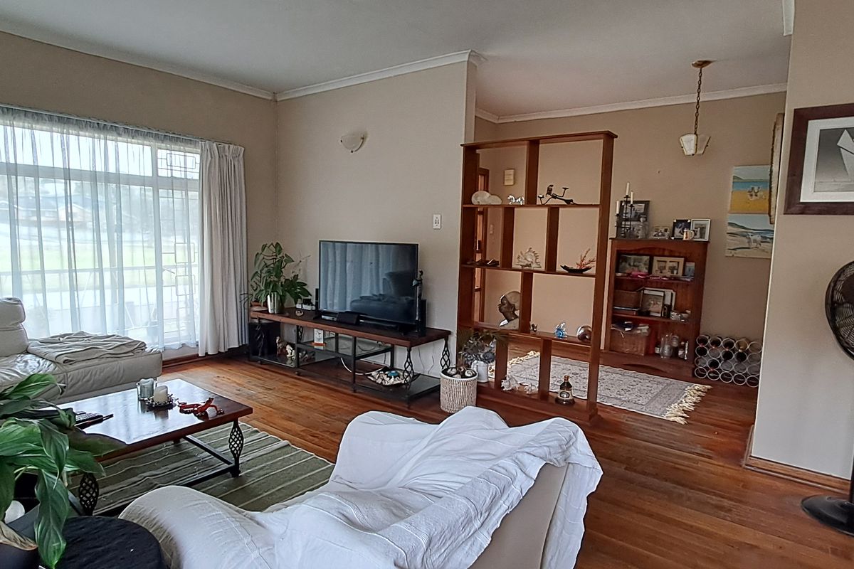 A spacious living room featuring warm hardwood flooring, large windows allowing natural light, and a functional open-plan layout with a room divider.