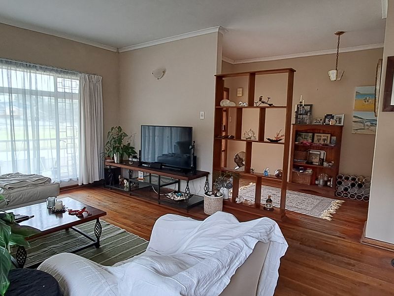 A spacious living room featuring warm hardwood flooring, large windows allowing natural light, and a functional open-plan layout with a room divider.