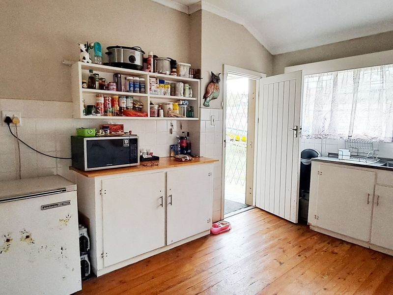 A functional kitchen featuring timber flooring, built-in cabinetry, a stainless steel sink, and direct access to the exterior.