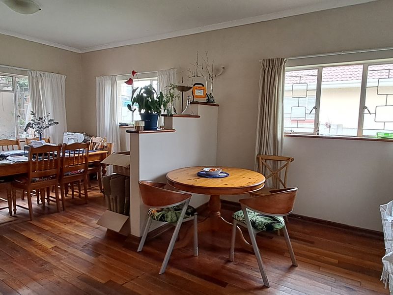 Open-plan living and dining area featuring warm hardwood flooring, a central partition wall, and large steel-framed windows providing natural light.