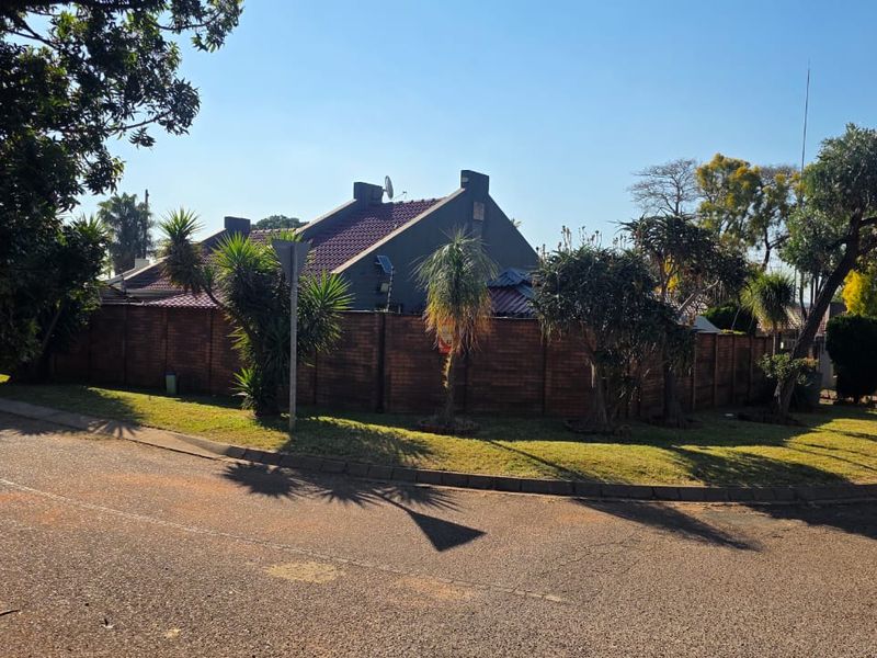 Street view of the property showing the corner lot, brick boundary wall, and tiled roof structure from the road.